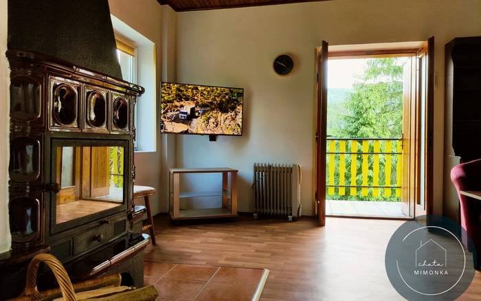 Obývacia izba s kachľovým krbom, TV a vstupom na balkón